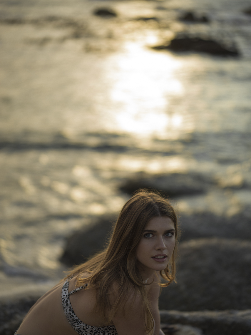Portrait of a female model in leopardskin print bikini crouched on rocks by the sea